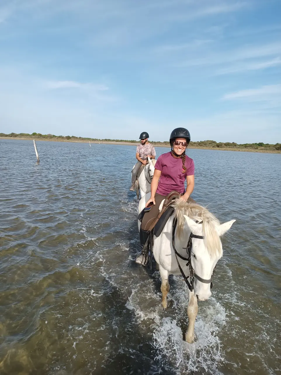 Balade à cheval dans un étang en Camargue - Expérience La Fadaise Cavalière souriante traversant un étang à cheval en Camargue avec La Fadaise, Saintes-Maries-de-la-Mer.